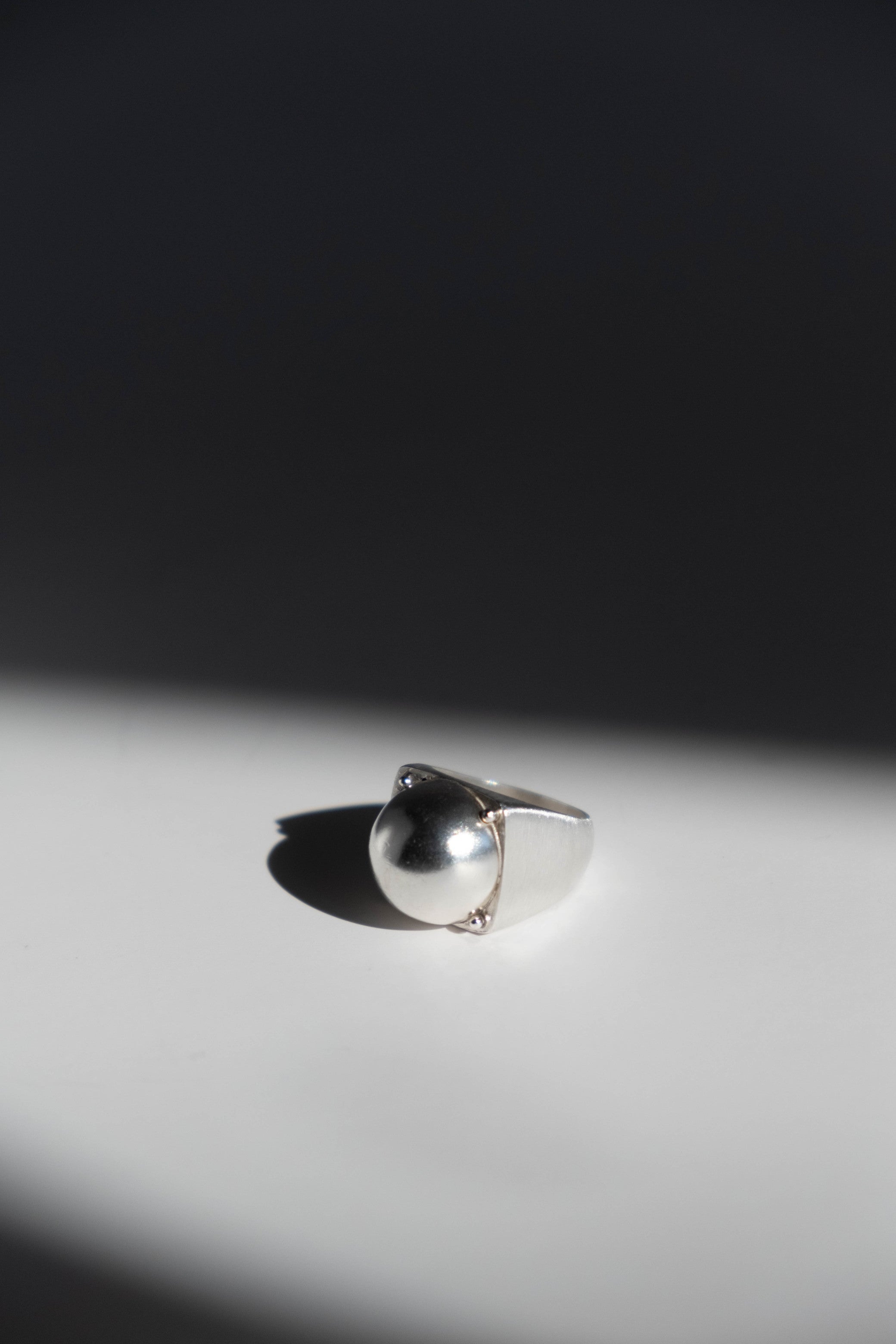 Silver ring on a light gray surface with a dark background
